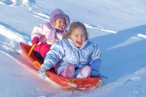 two kids sliding down snow hill on suacer